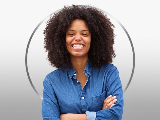 Mulher sorridente com cabelo encaracolado, que está a usar uma blusa azul e satisfeita depois de ter experimentado o tratamento da Canesten para a candidíase